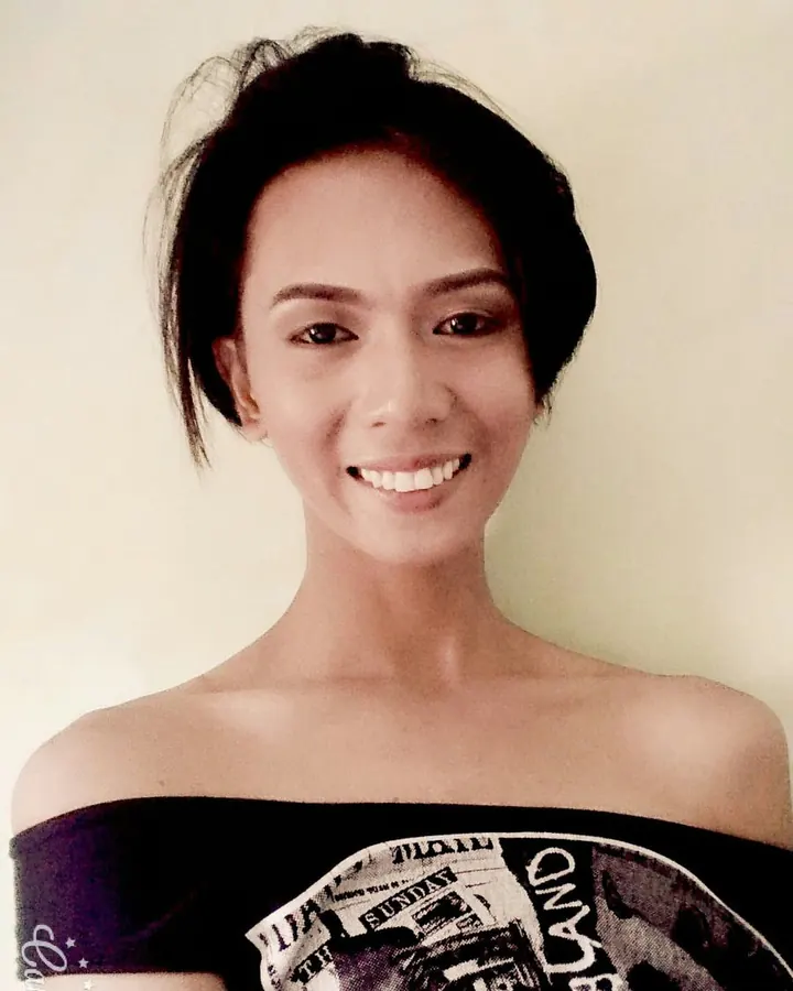 Jeune femme latine aux cheveux bruns-noirs, vêtue d'un haut noir et d'une jupe rayée, prenant un selfie dans un miroir.