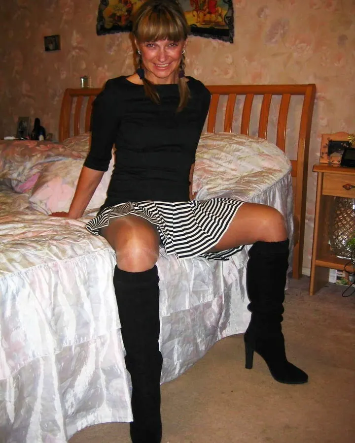Femme en robe noire et jupe rayée, assise sur un lit