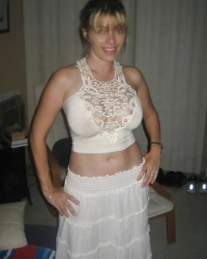 Femme aux cheveux blonds, vêtue d'une tenue blanche et grise, posant devant un miroir, prenant un selfie.