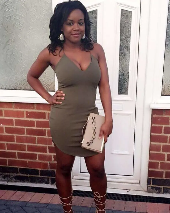 Femme souriante portant une robe verte, tenant un sac à main, debout devant une porte blanche.