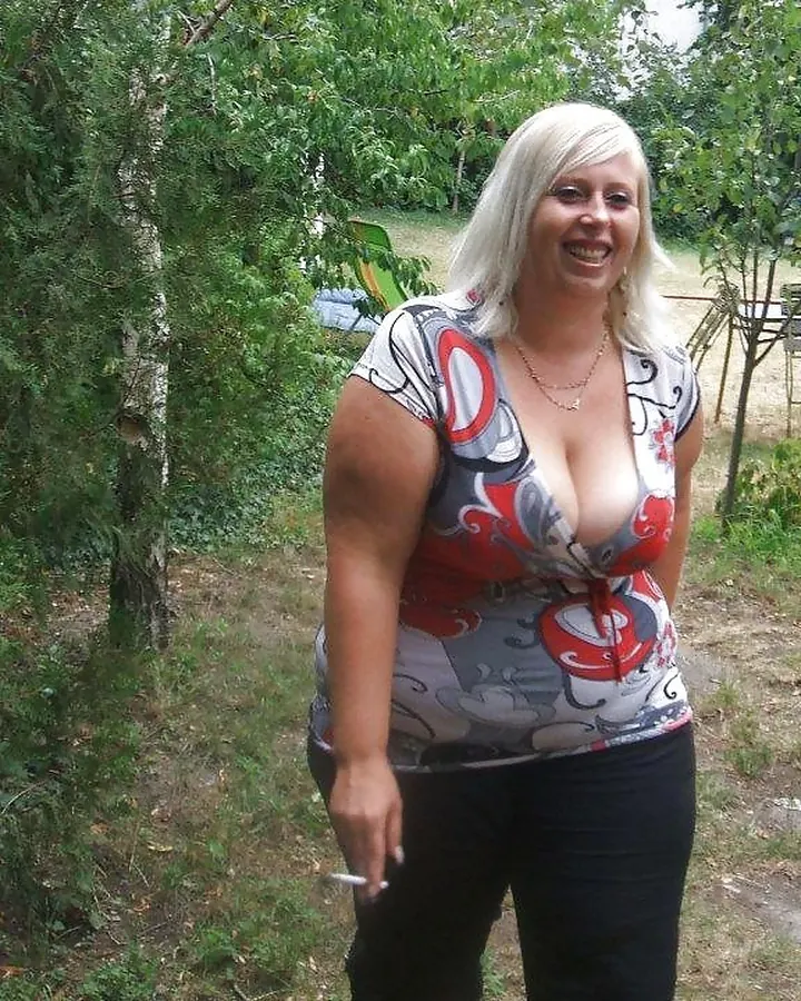 Femme blonde aux cheveux blancs, portant une tenue noire en latex, posant dans une pièce aux murs violets.