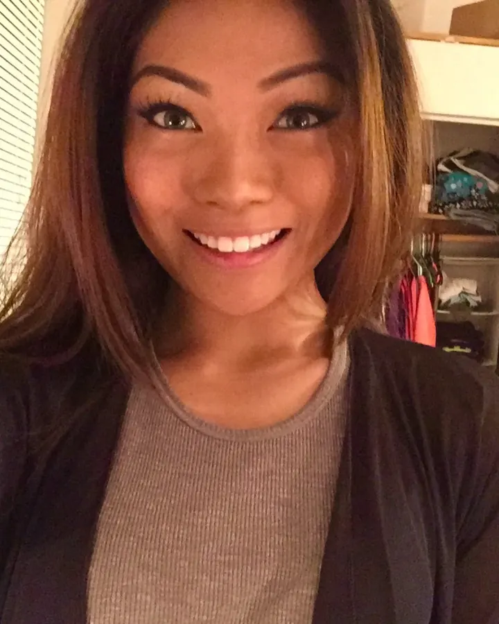 Femme asiatique aux cheveux bruns, souriante, en tenue décontractée, prenant un selfie dans une chambre.