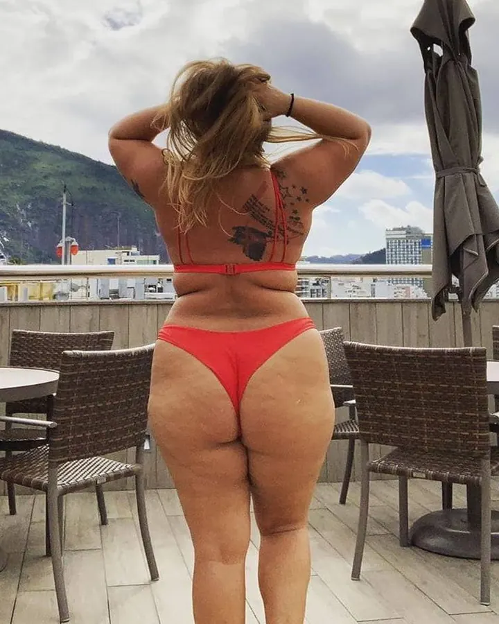 Femme blonde aux cheveux blonds portant un maillot de bain rouge, de dos, sur une terrasse avec vue sur la montagne.