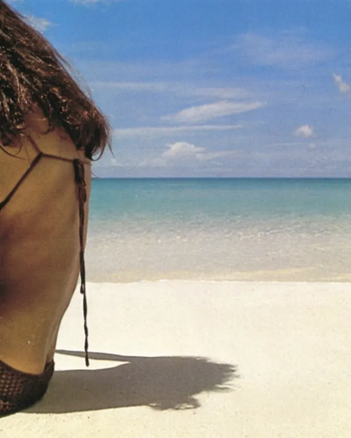 Jeune femme aux cheveux châtains portant un maillot de bain rose, posant devant une végétation luxuriante.