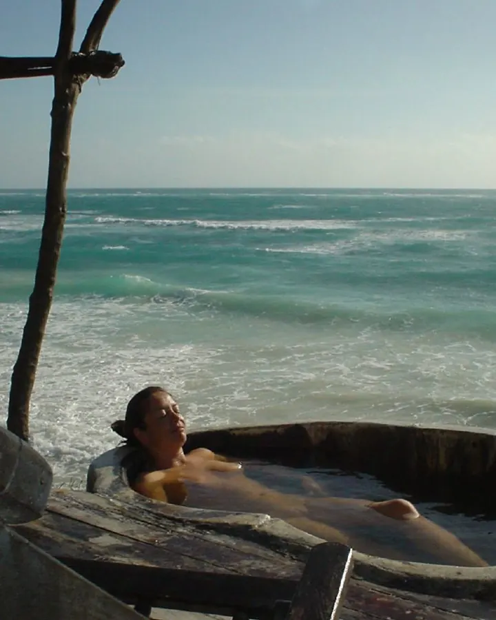 Femme aux cheveux bruns portant un maillot de bain noir, posant de dos près d'une piscine.