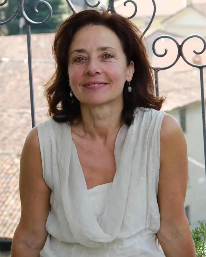 Femme européenne aux cheveux châtains, en robe rouge, posant dans une pièce, main sur la hanche, regardant vers le bas.