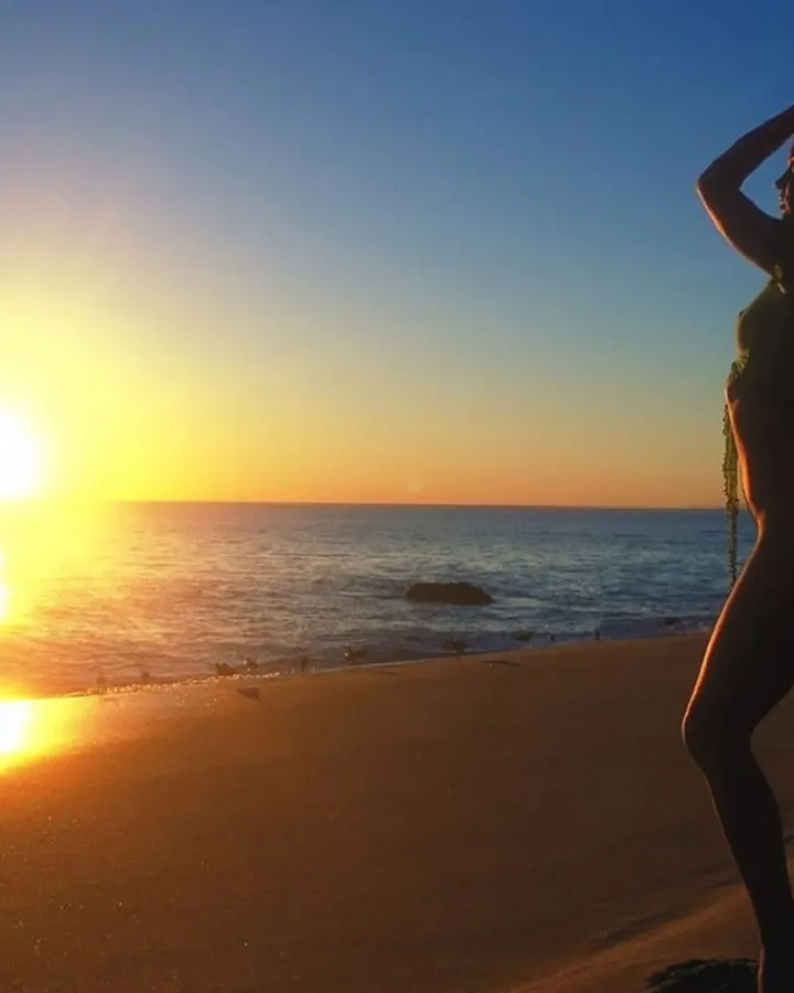 Silhouette féminine sur une plage au coucher du soleil, les mains dans les cheveux.
