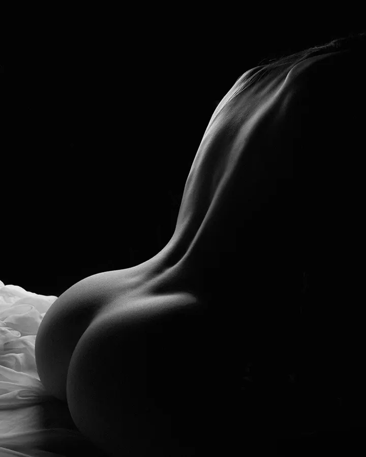 Photo en noir et blanc d'une silhouette féminine en position couchée, mettant en valeur la courbe du dos et des fesses.