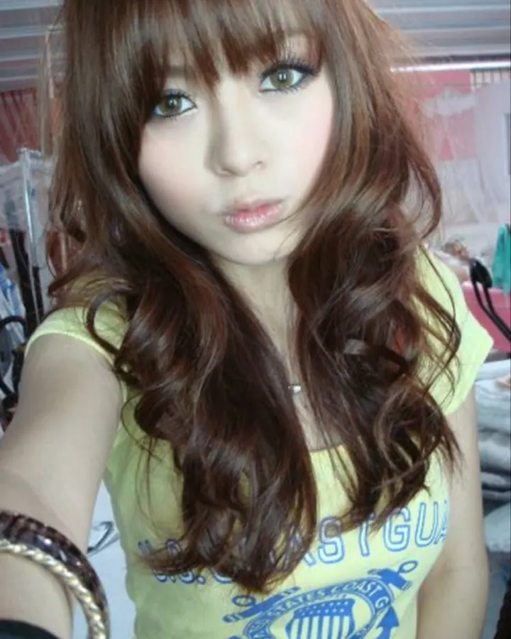 Jeune femme aux cheveux bruns, regardant vers le haut, en chemisier jaune, prenant un selfie.