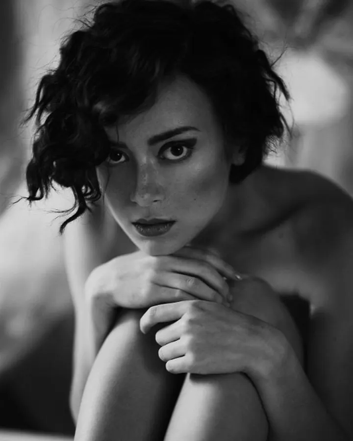 Femme en noir et blanc, assise, les genoux repliés, regardant directement l'appareil.
