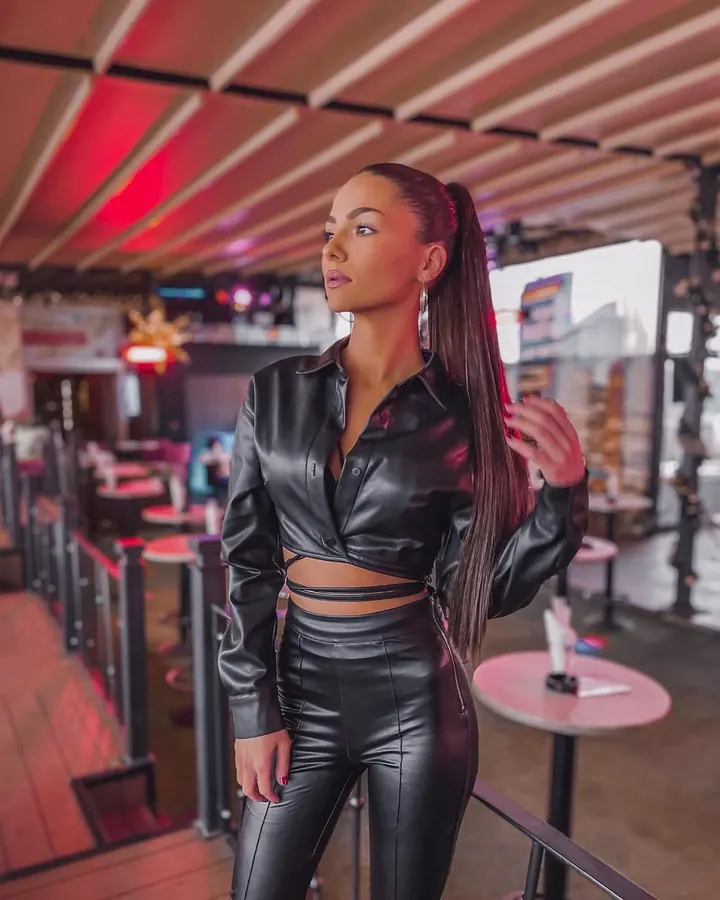 Femme en tenue de sport bleue, appuyée contre un mur blanc, regardant vers le bas.