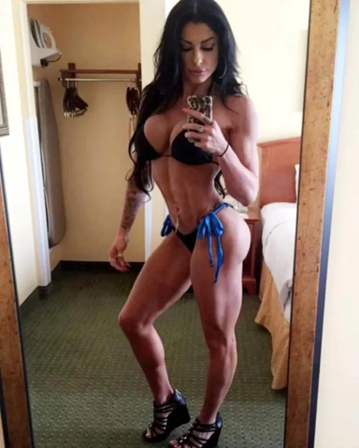 Femme aux longs cheveux noirs en bikini noir, prenant un selfie devant un miroir dans une chambre d’hôtel.