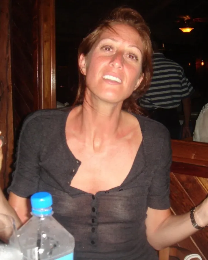 Femme aux cheveux châtains assise dans un restaurant, portant un haut sombre à boutons, souriant légèrement.