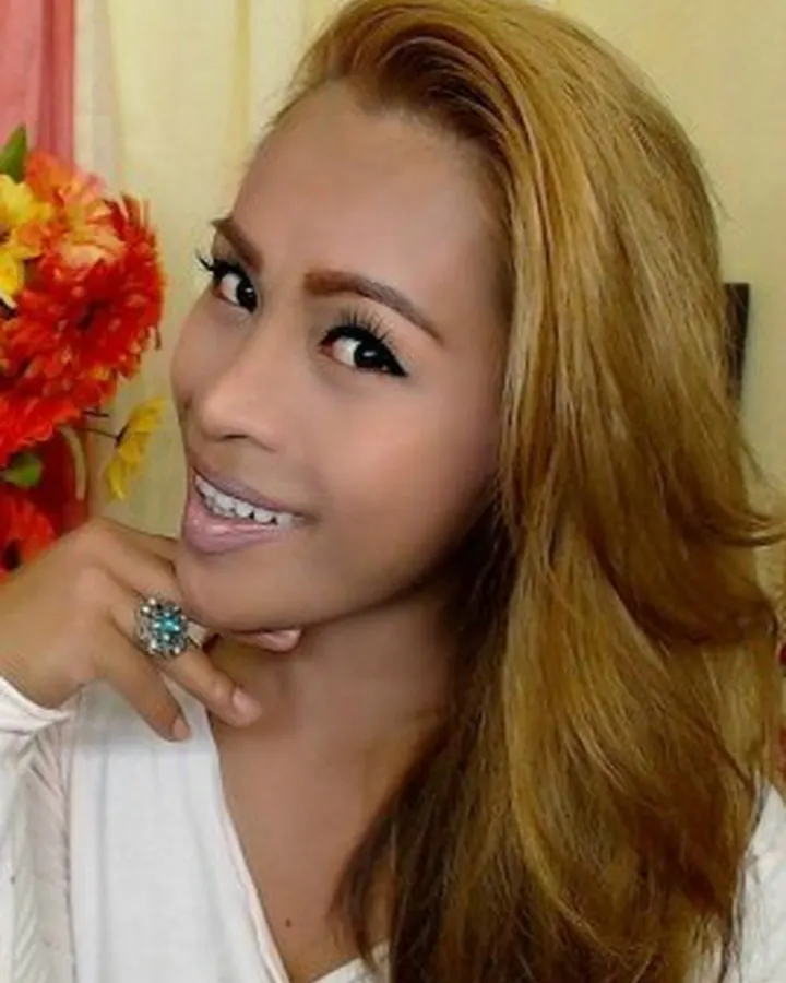 Femme en robe blanche, posant de profil avec un bouquet de fleurs rouges et jaunes.