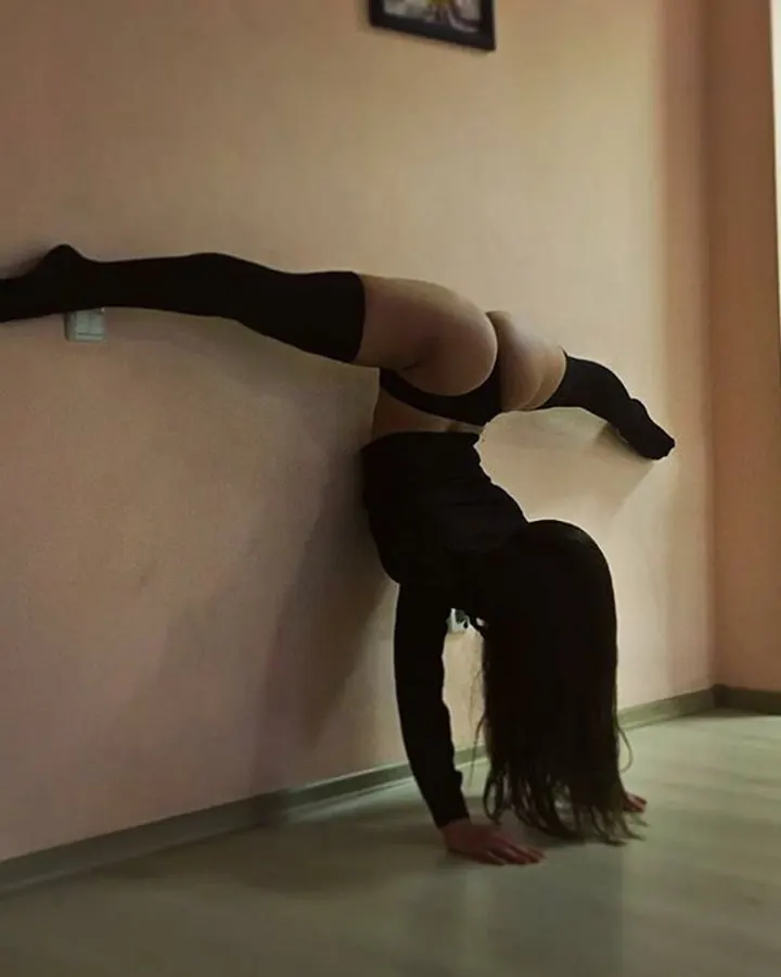Femme en position de flexion contre un mur, en tenue noire, les cheveux longs.