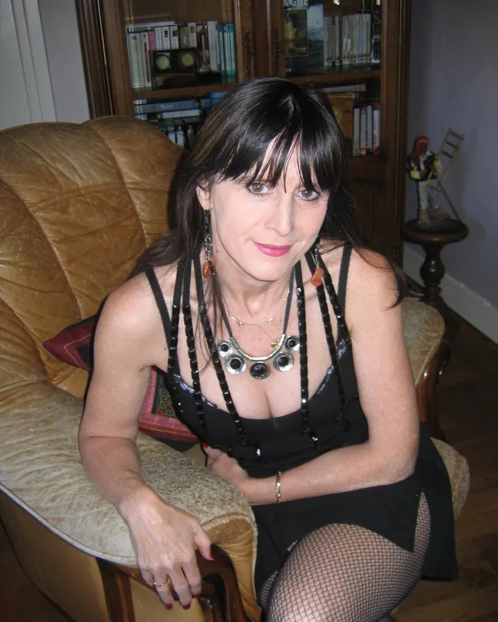 Femme aux cheveux bruns, vêtue d'un haut noir et d'une jupe noire, assise dans un fauteuil en cuir marron.