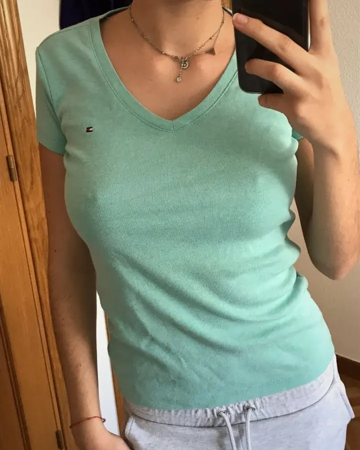 Femme en t-shirt vert, prenant un selfie devant un miroir, tenant un téléphone noir.