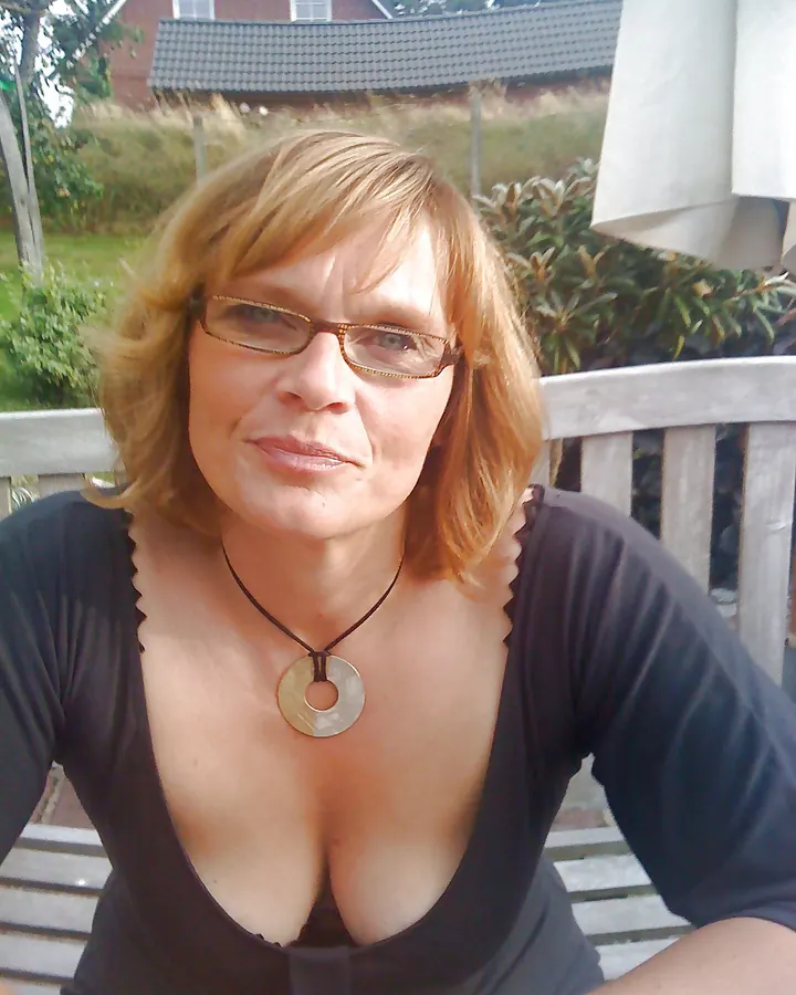 Femme aux cheveux blonds, portant un haut noir, les bras levés, tatouages visibles sur les bras et le torse.
