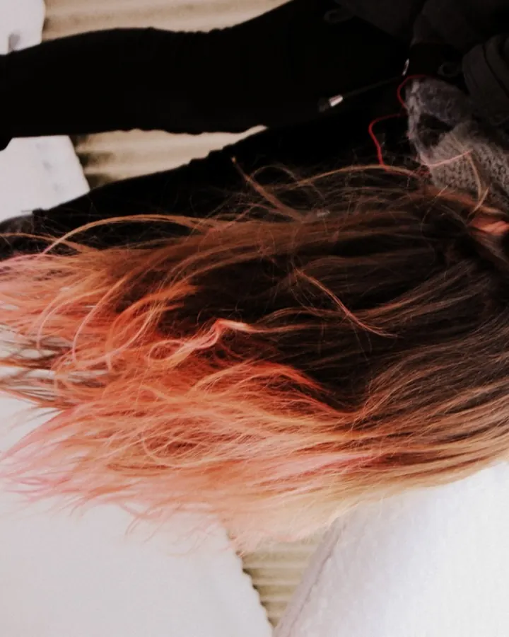 Femme aux cheveux roux longs, portant un haut noir à décolleté profond, assise sur un canapé orange dans un salon.