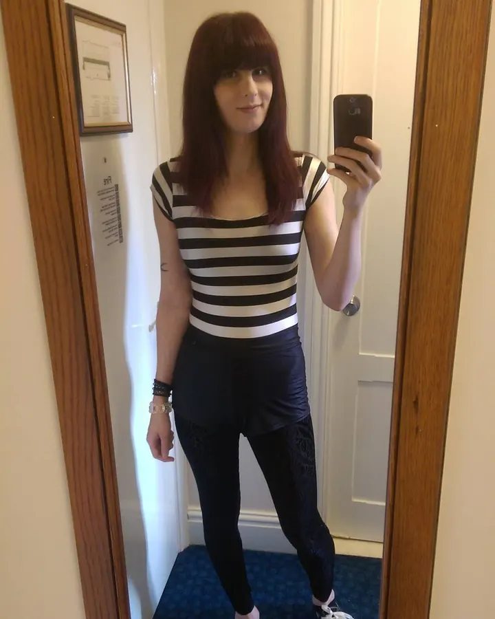 Jeune femme aux cheveux châtains, en sous-vêtements roses, prenant un selfie devant un miroir dans une chambre.
