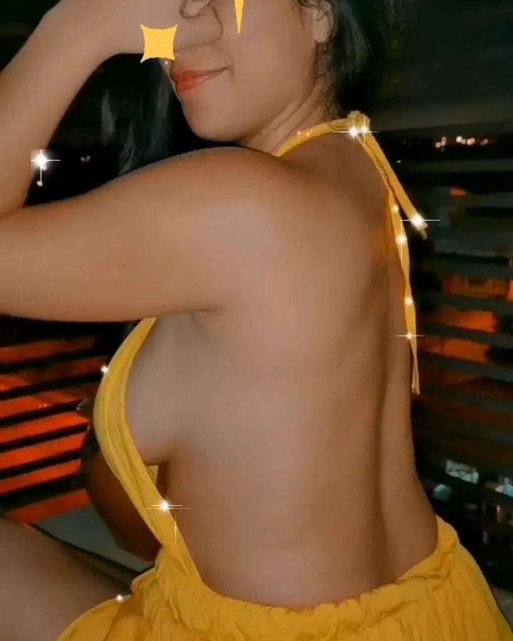 Femme aux cheveux noirs en haut jaune, posant de profil dans un cadre sombre avec des effets lumineux.