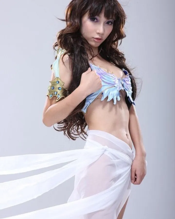 Jeune femme asiatique en tenue de déesse, bustier bleu irisé et drapé blanc, pose devant fond gris.