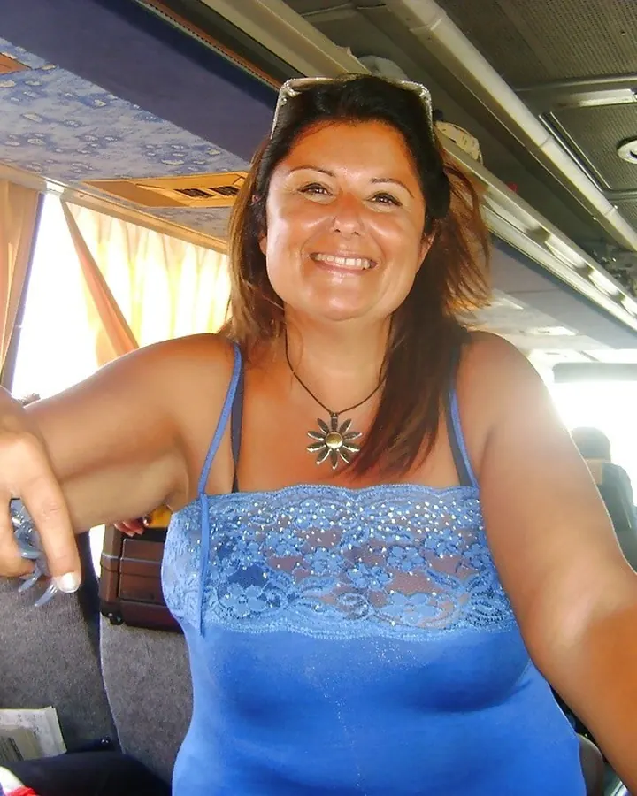 Femme aux cheveux bruns portant une robe bleue, souriant à l’intérieur d’un bus.