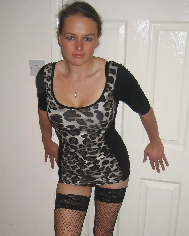 Femme en robe noire à motifs léopard, collants résille et bas noirs, posant devant une porte blanche.