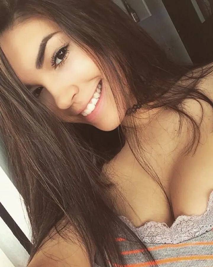 Femme aux cheveux bruns foncés, souriante, en haut à dentelle blanche et rayures colorées.