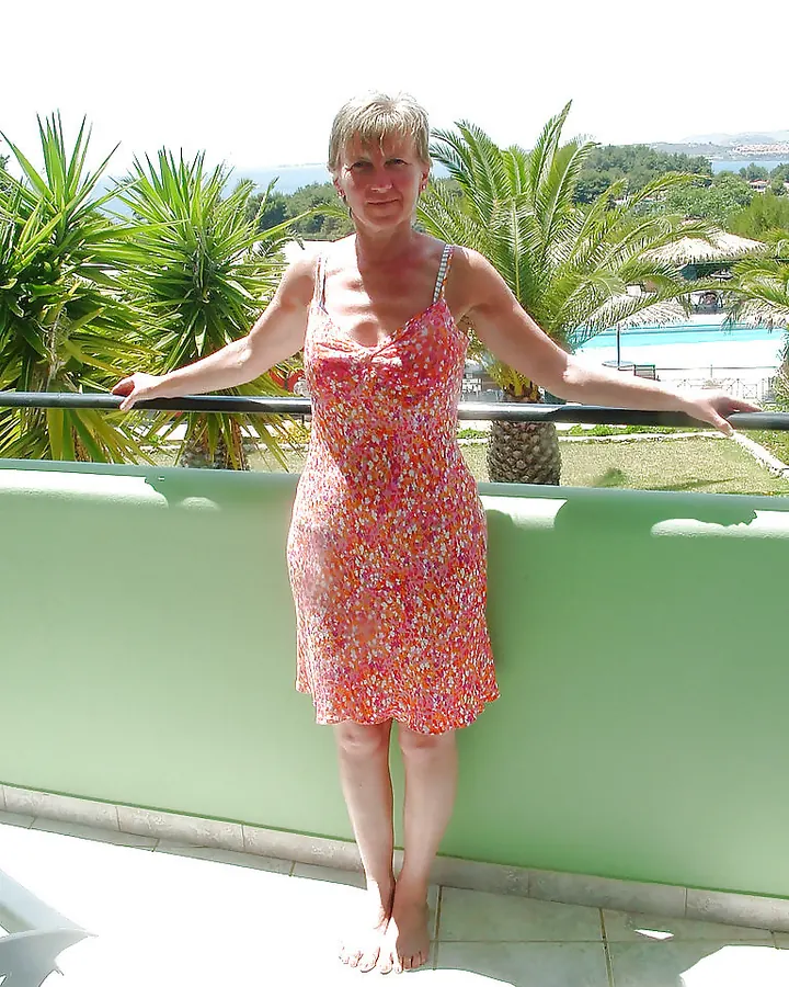 Femme en robe fleurie rose, debout sur balcon avec vue sur mer et palmiers