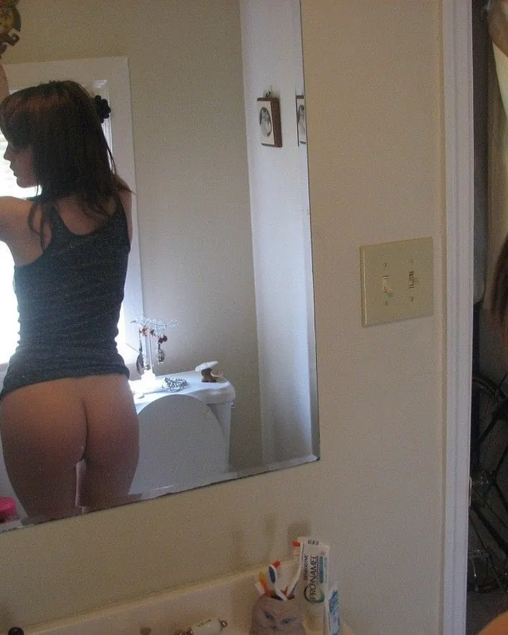 Femme brune vue de dos devant miroir, appareil photo en main