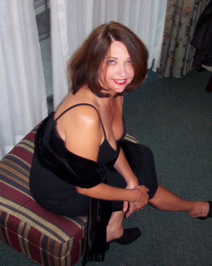 Femme aux cheveux roux en lingerie noire, posant sur un canapé rayé.