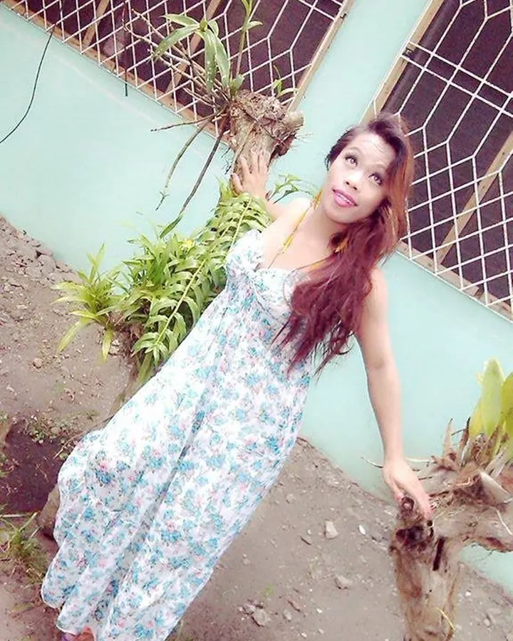 Femme aux cheveux châtains en robe fleurie, posant dans un jardin.