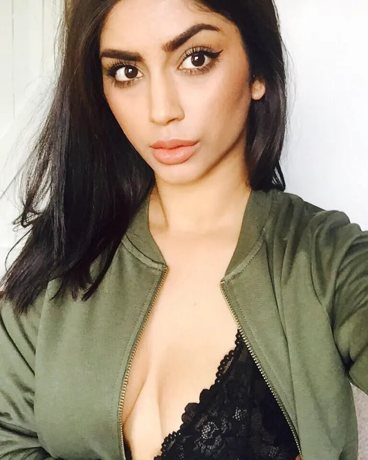 Femme aux cheveux noirs, vêtue d'une veste verte et d'un soutien-gorge noir en dentelle, prenant un selfie.