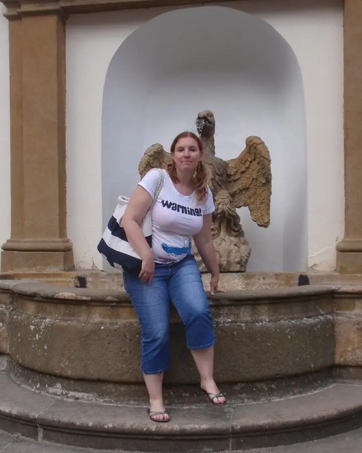Femme aux cheveux blonds, en robe bleue, posant sur un escalier.