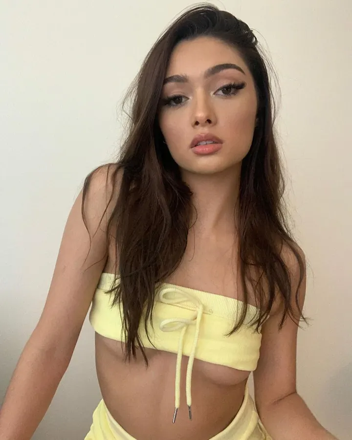 Femme en haut jaune sans bretelles, posant de face avec des cheveux bruns longs.